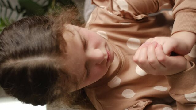 Vertical footage of cute little girl sitting on cozy sofa at home keep hands in prayer hope believe ask good luck, hopeful pretty child believer pray do religious superstitious gesture, faith concept