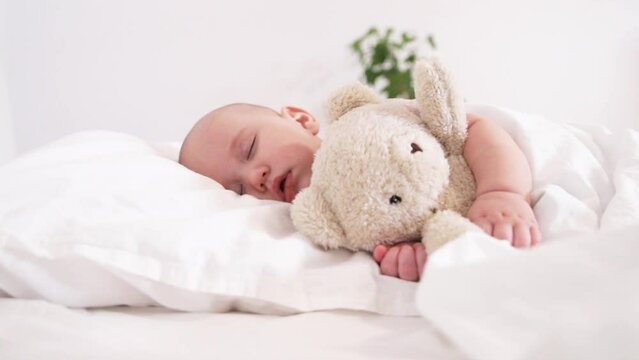 Adorable child holding teddy bear sleeping sweetly on white bed on greenery background diapers advertisement