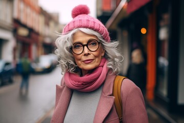 Beautiful senior woman in pink hat and scarf walking on the street - obrazy, fototapety, plakaty