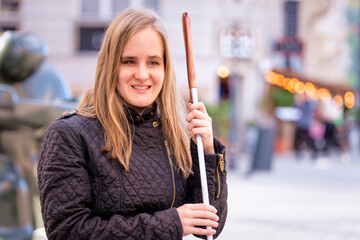 A visually impaired woman holding a white cane and sitting on a bench in the city