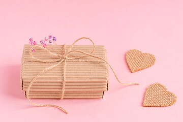 Craft handmade carton disposable gift box tied up with string bow decorated with dried gypsophila flowers on pink background with heart shaped decoration used as recyclable present for celebration