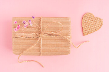Top view of craft handmade carton recyclable gift box tied up with string bow decorated with dried gypsophila purple flowers on pink background with heart shaped decoration used for holiday present