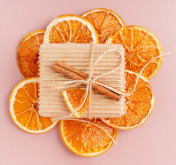 Top view of craft carton recyclable gift box tied up with string bow decorated with dried citrus slice and cinnamon stick on sliced ornage fruit on brown background used as holiday present decor