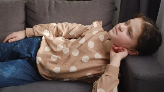Relaxed dreamful cute little girl child lying on comfortable sofa in living room at home. Portrait of adorable preteen kid smiling and relaxing on cozy couch, enjoying weekend. Concept childhood