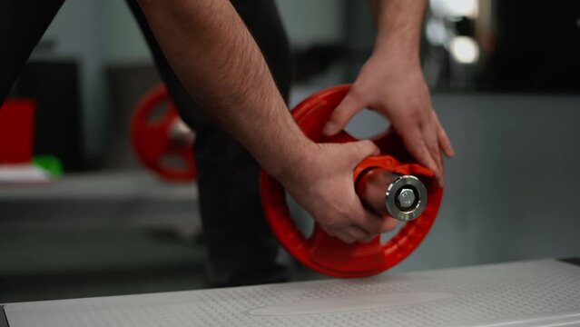 The athlete puts a locking nut on the barbell. Close-up of the hand in the frame. Concept: safe exercise in the gym.