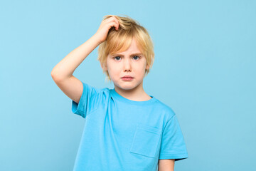 Young doubtful confused boy thinking, scratching head, trying to find solution, isolated on pastel blue background.