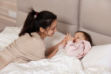 happy mother playing with her cute baby daughter on bed in bedroom. loving family having fun