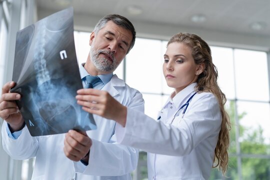 Professional medical team with doctors and surgeon examining patient's x-ray image, discussing and pointing.