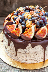Delicious cake with figs dipped into melted chocolate, pecan nuts, grapes, chocolate bites and cookies on the top on rustic background