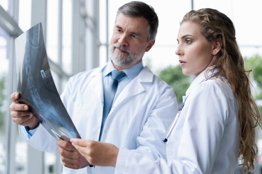 Professional medical team with doctors and surgeon examining patient's x-ray image, discussing and pointing.