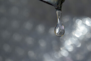 Detail of small water drop coming out of dripping faucet with bright background horizontally
