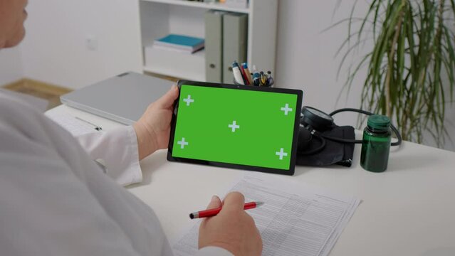 Gadget tablet with green screen hold by medical assistant. Doctor workplace, woman nurse working. Distance education, e-learning.