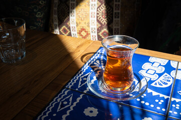 Figured glass Armudu with tea in a Georgian restaurant. The glass stands in a ray of sun. in the background there are large colorful pillows with hand embroidery