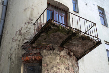 dangerous balcony in an old residential building. The concrete slab is almost destroyed, exposing rusty reinforcement. The plaster of the wall is also damaged exposing the brickwork