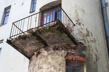 dangerous balcony in an old residential building. The concrete slab is almost destroyed, exposing rusty reinforcement. The plaster of the wall is also damaged exposing the brickwork