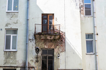 dangerous balcony in an old residential building. The concrete slab is almost destroyed, exposing rusty reinforcement. The plaster of the wall is also damaged exposing the brickwork