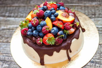 Delicious cheesecake with melted chocolate, apples, strawberries, blueberries, peaches, raspberries and kumquats on the top, rustic background