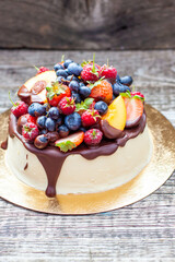 Delicious cheesecake with melted chocolate, apples, strawberries, blueberries, peaches, raspberries and kumquats on the top, rustic background