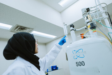 Muslim Scientist Standing in Front of NMR Machine, Pointing towards the Equipment