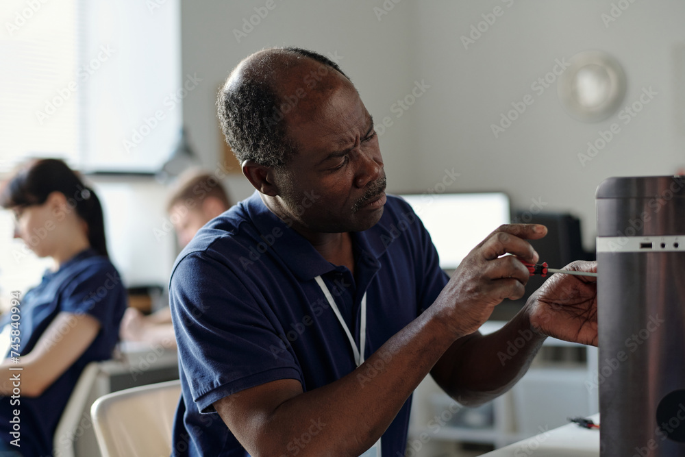 Poster serious mature african american male engineer of repair service center unfixing parts of computer pr