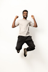 Energetic African American man in casual attire leaping joyfully against a white studio background, expressing freedom and happiness. - 745840968