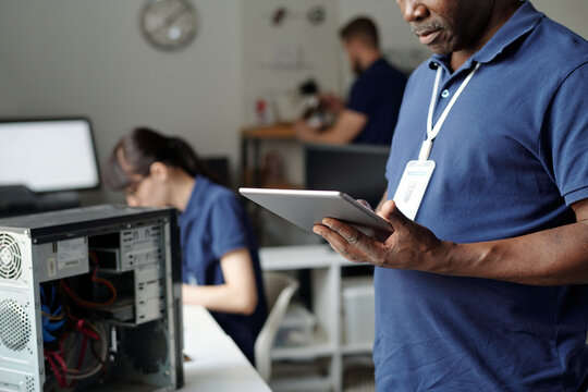 African American male technician of repair center holding tablet and looking through online instruction on screen in coworking space