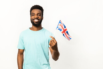 Joyful African American male showcasing patriotism by holding a small United Kingdom flag, isolated on a white background, expressing positive emotions and cultural pride. - 745843935