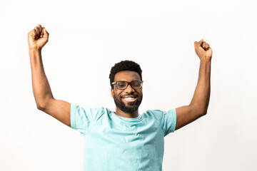 African American man with glasses raises his fists in a triumphant cheer, expressing success and...