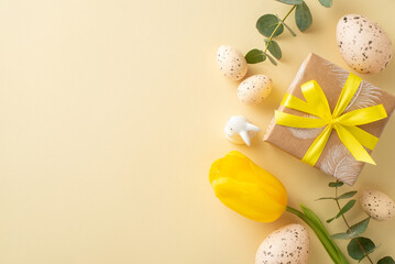 Charming Easter table setting idea. Top view shot featuring brown craft paper present, yellow tulip, eucalyptus, rabbit figurine, speckled quail eggs, laid out on light beige backdrop, space for copy