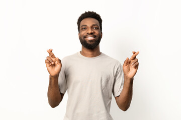 Portrait of a cheerful man crossing fingers for good fortune, smiling against a white background with positive vibes. - 745844947