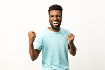Energetic African American male cheering with clenched fists in a triumphant gesture on a plain background. - 745845159