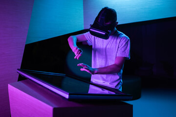 Young man with a VR headset having an immersive virtual reality experience in a room with purple lighting, making various hand movements in the air.