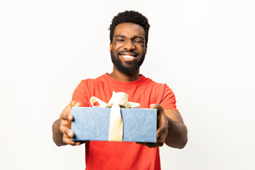 Cheerful African American man presenting a wrapped gift box with a joyous smile, isolated on a white background. Concept of celebration, generosity, and sharing. - 745846376