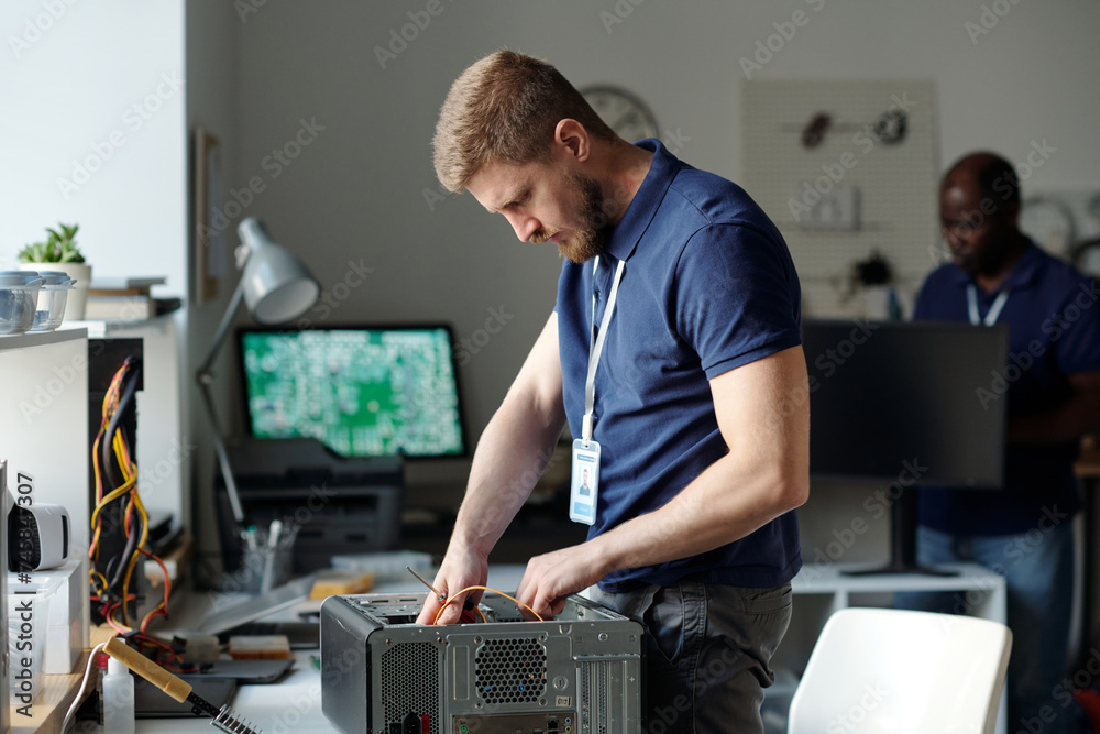 Aufkleber young technician checking details of disassembled computer processor while bending over desk with ha