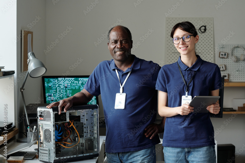 Poster two successful engineers of repair service center looking at camera while young woman using tablet a