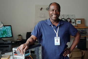 Mature African American experienced technician in blue shirt keeping arm on top of computer...