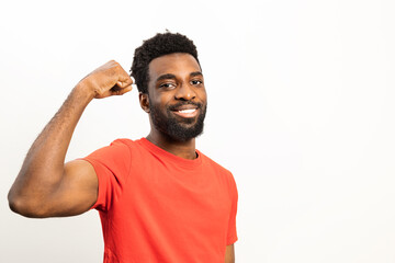 Portrait of a cheerful African American man in a vibrant red shirt flexing his muscles and smiling,...