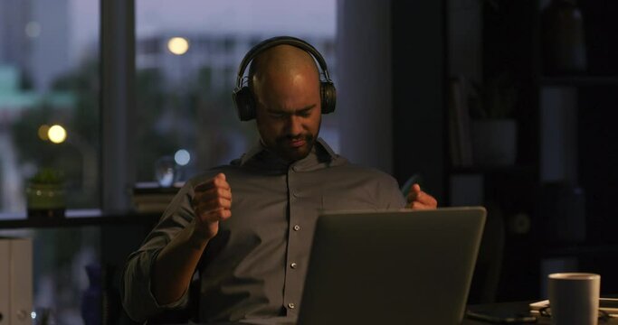 Night, headphones or businessman in office dancing to music for online radio streaming service. Celebration, worker or employee listening to gospel song in workplace in overtime with air guitar
