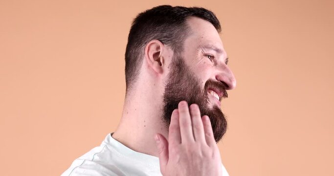 Handsome bearded man holding beard balm and applies on beard beige background.