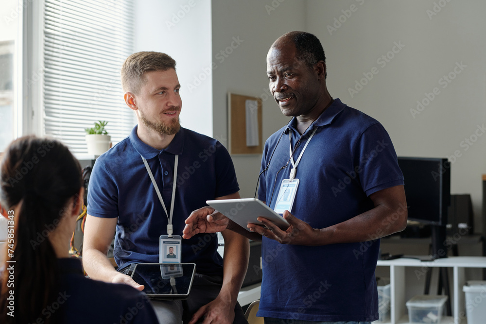 Aufkleber confident mature businessman with tablet looking at one of young subordinates during explanation or 