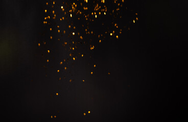 Golden confetti sparkling against a stark black background, creating a striking contrast and...