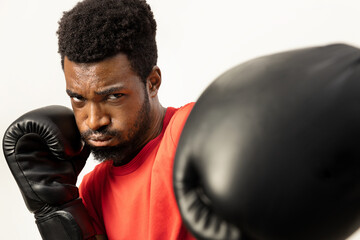 A young, focused African American man is captured in a dynamic boxing stance, wearing gloves, exuding confidence and determination, isolated on a white background. - 745851954