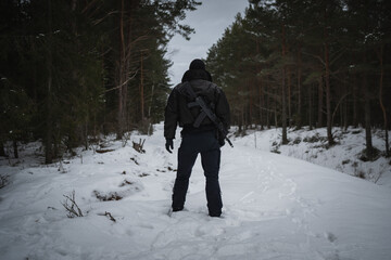 A private military man with an rifle behind his back in a winter forest, photo from the back.