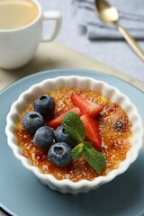 Delicious creme brulee with berries and mint in bowl on table, closeup