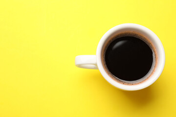 Fresh coffee in cup on yellow background, top view. Space for text