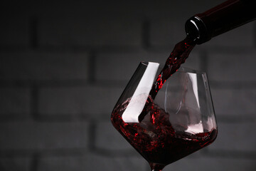 Pouring tasty red wine from bottle into glass against brick wall, closeup. Space for text