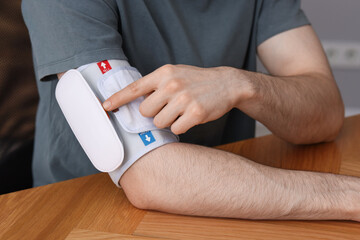 Man measuring his blood pressure with tonometer at wooden table indoors, closeup
