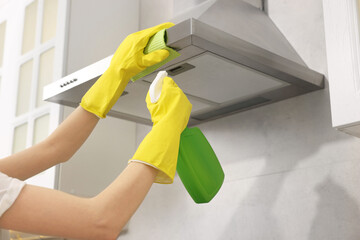 Woman with spray bottle and microfiber cloth cleaning kitchen hood indoors, closeup