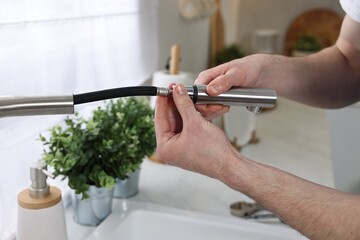 Plumber examining metal faucet at home, closeup