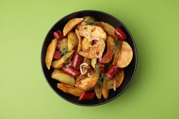 Delicious baked potato with thin dry smoked sausages, onion and dill in bowl on green table, top view